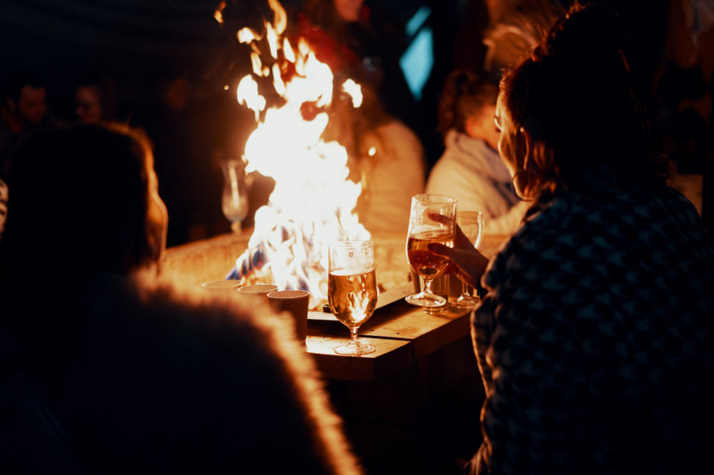 Group of people huddled around a fire pit drinking cocktails